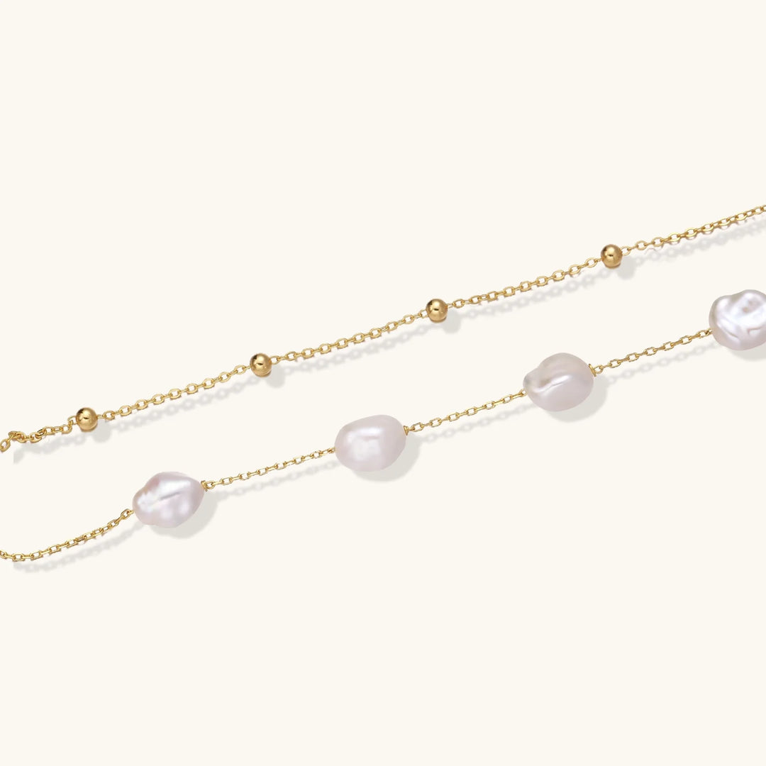 Double-strand gold bracelet with irregular baroque pearls and smooth freshwater pearls on cream background.