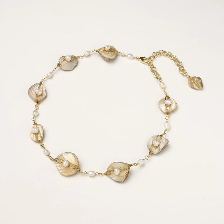 Gold-plated necklace with wire-wrapped shell pieces and freshwater pearls on neutral background, adjustable chain visible.