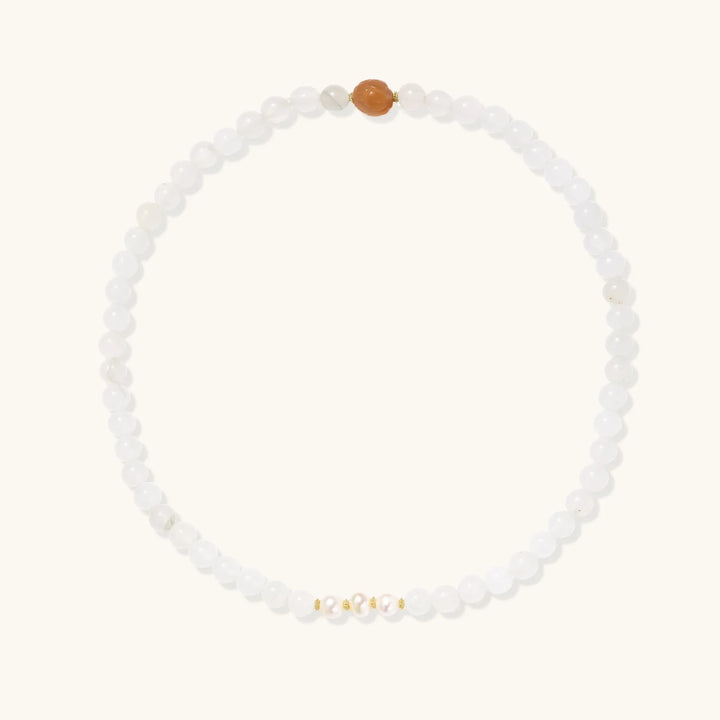 Three layered white beaded bracelets with carved orange agate lotus centerpiece and freshwater pearls on cream background.