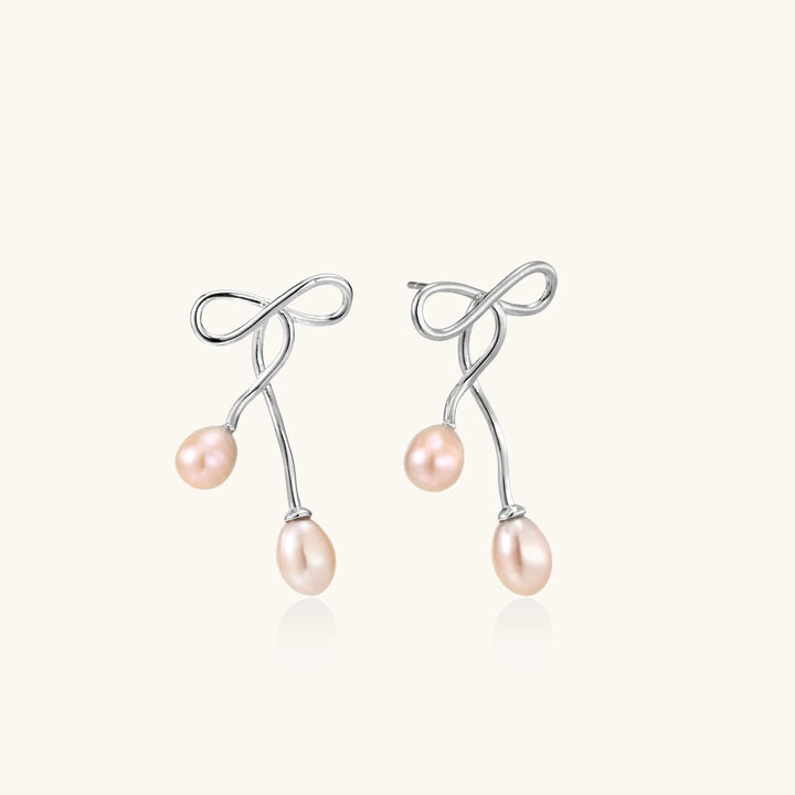 Rhodium-plated silver earrings with organic vine curves and two peachy freshwater pearls on cream background