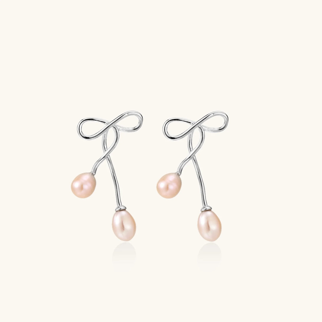 Rhodium-plated silver earrings with organic vine curves and two peachy freshwater pearls on cream background