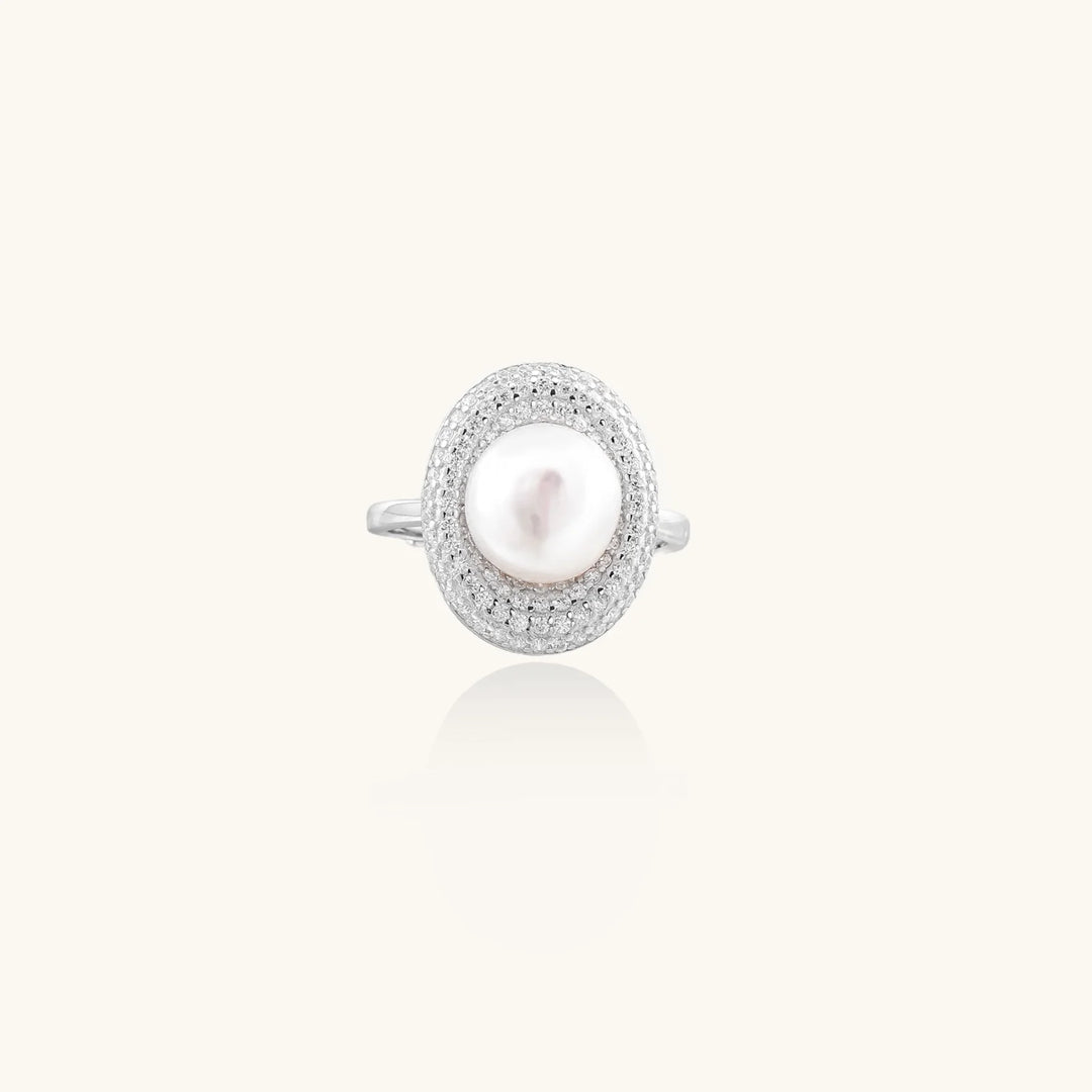 Silver ring with lustrous white pearl center surrounded by sparkling crystal halo on light background.