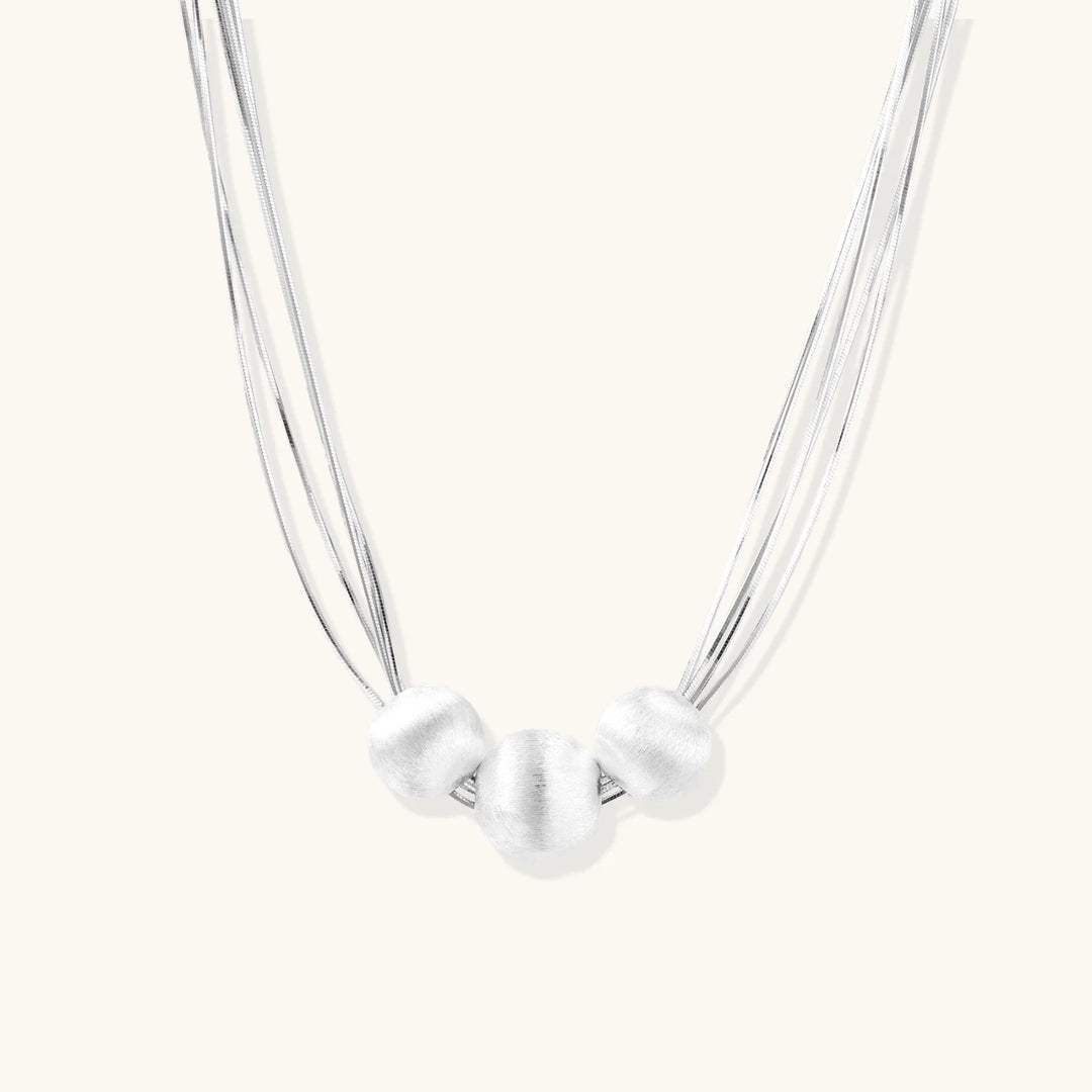 Sterling silver multi-strand necklace with three brushed round beads on cream background
