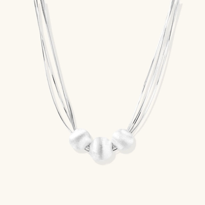 Sterling silver multi-strand necklace with three brushed round beads on cream background