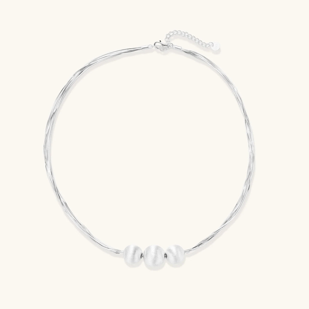 Sterling silver multi-strand necklace with three brushed round beads on cream background