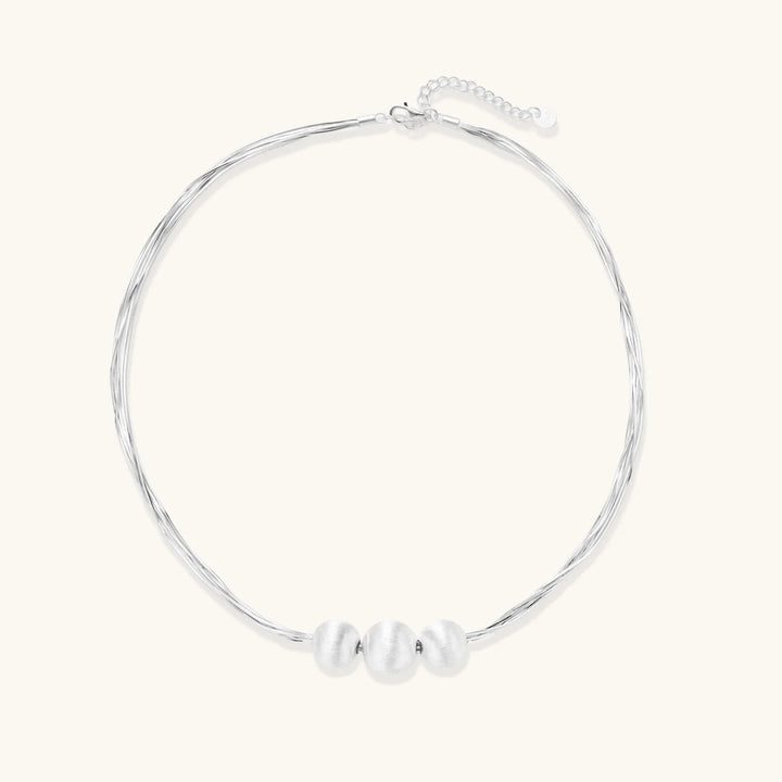 Sterling silver multi-strand necklace with three brushed round beads on cream background