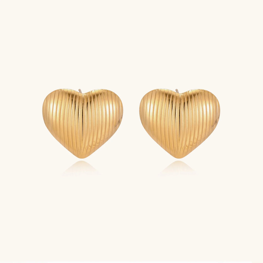 Gold heart-shaped stud earrings with parallel ridged texture on cream background