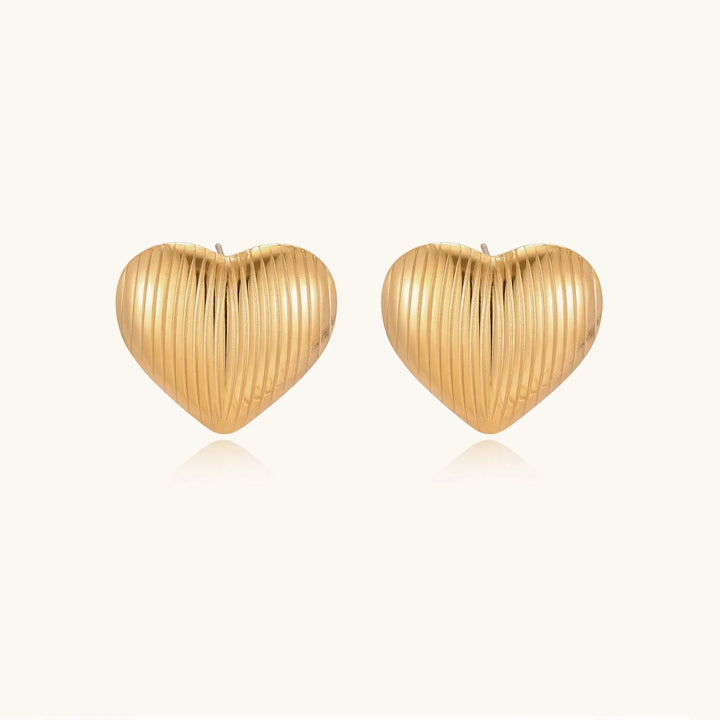 Gold heart-shaped stud earrings with parallel ridged texture on cream background