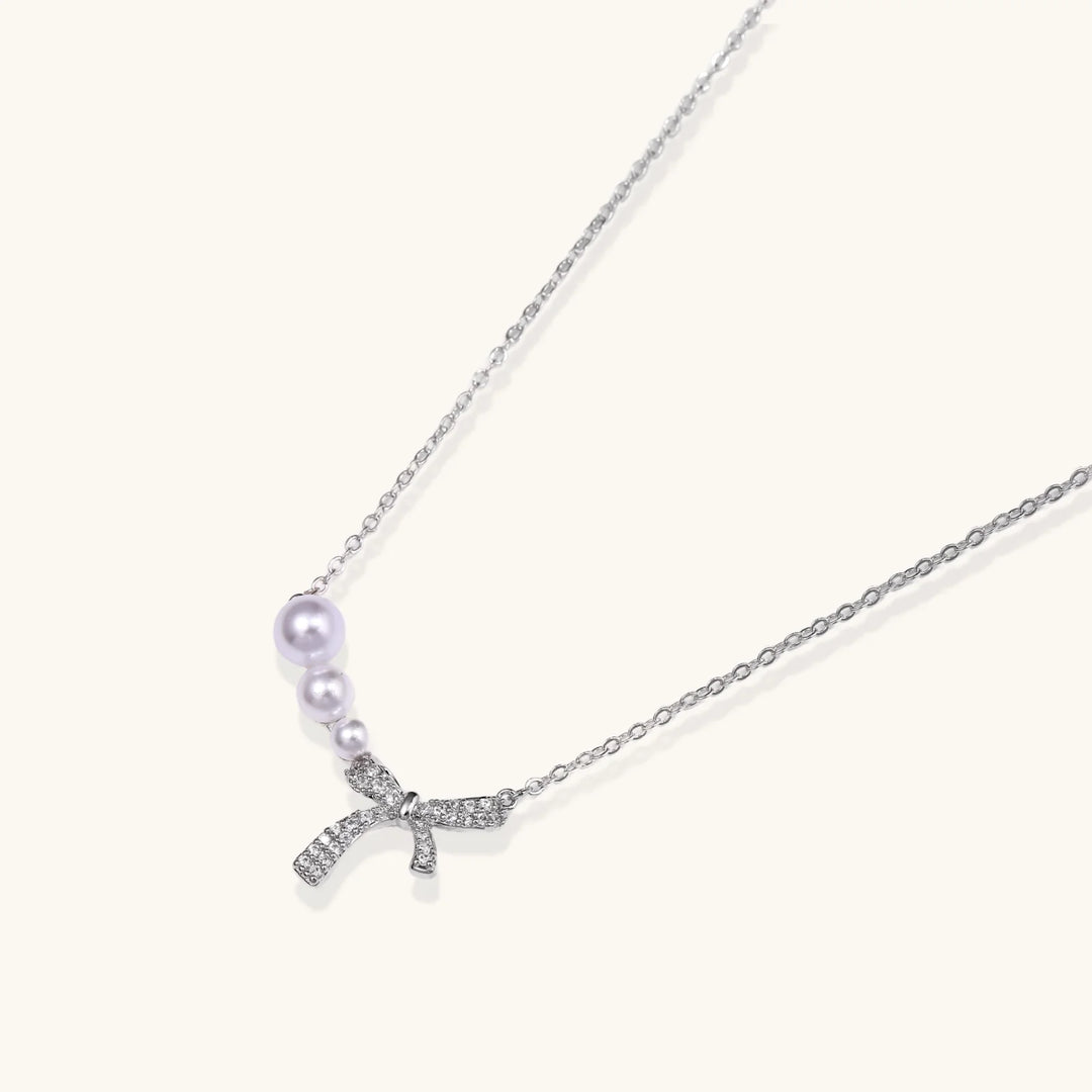 Delicate white gold plated necklace with graduated freshwater pearls and crystal-studded bow pendant on ivory background