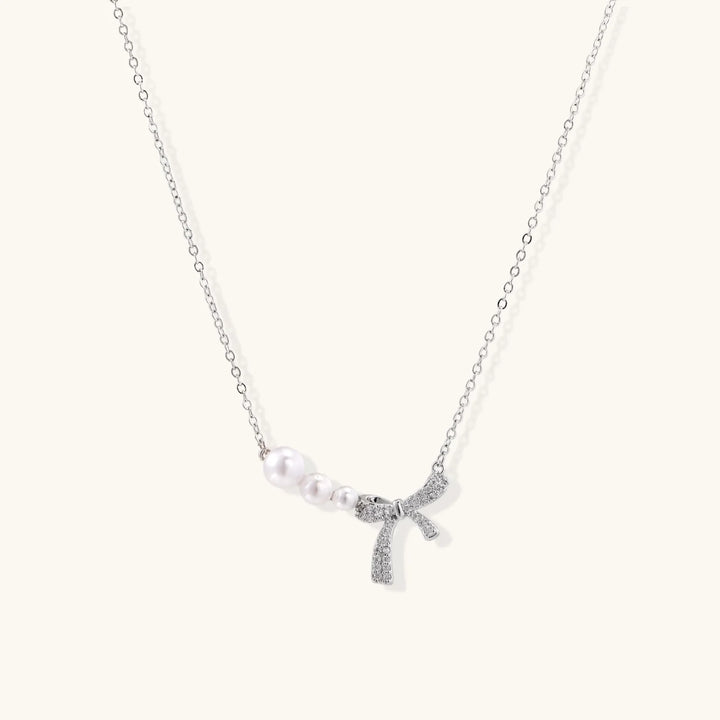 Delicate white gold plated necklace with graduated freshwater pearls and crystal-studded bow pendant on ivory background
