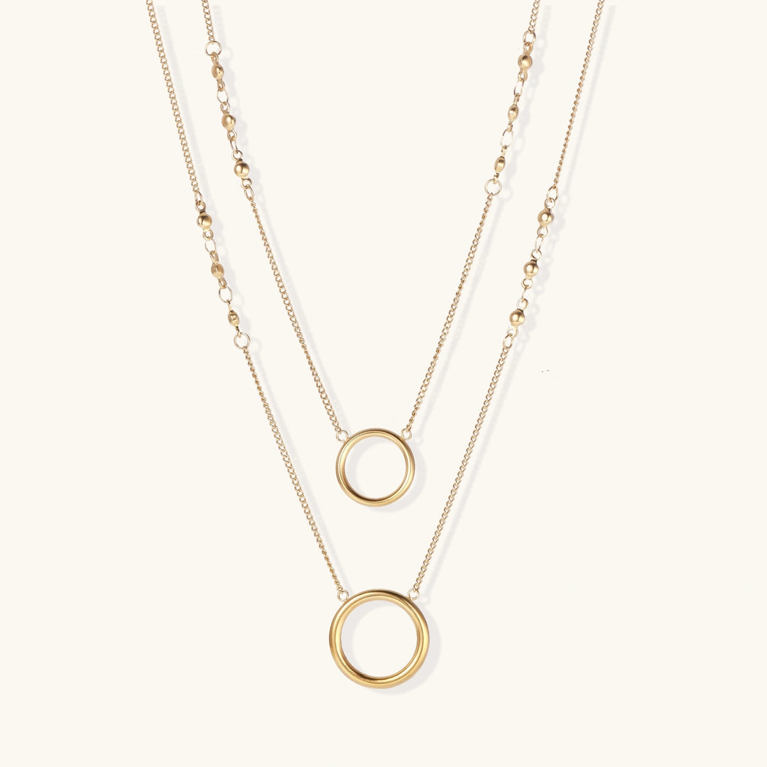 Layered gold necklace set with two open circle pendants and mixed chain styles on beige background
