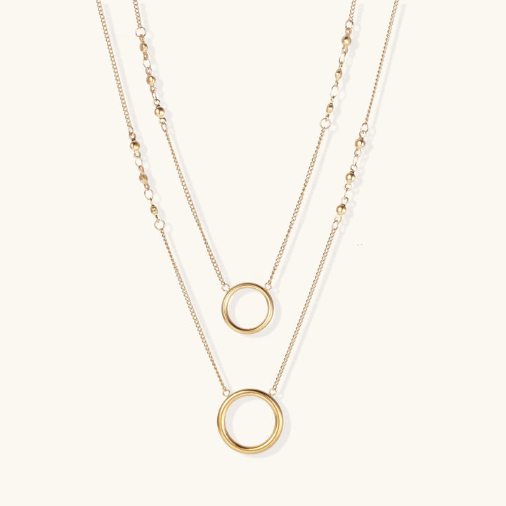 Layered gold necklace set with two open circle pendants and mixed chain styles on beige background