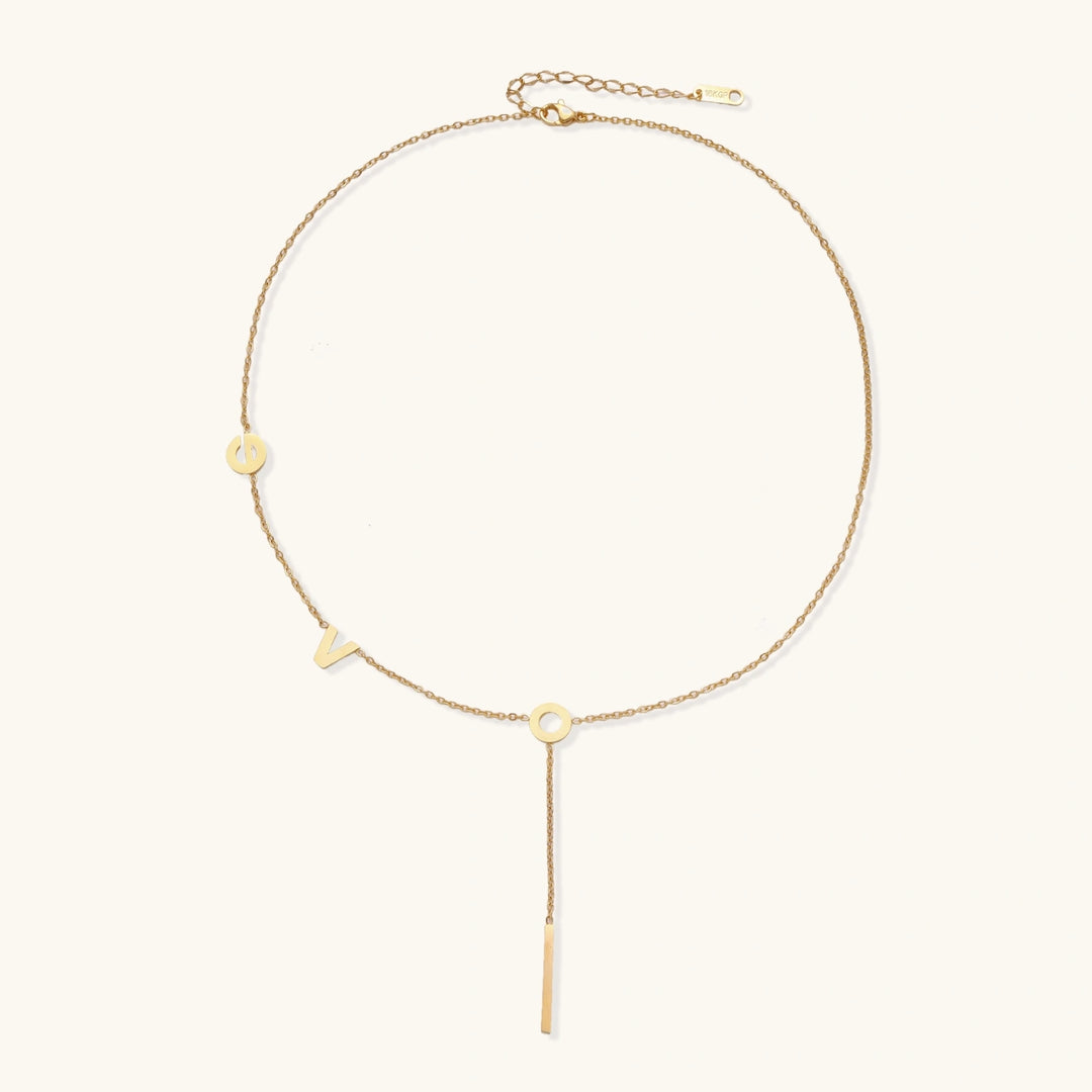Gold Y-shaped necklace with L-O-V-E letter charms and vertical bar pendant on delicate chain against cream background