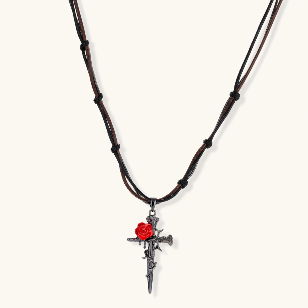 Gothic cross pendant with red enamel rose and thorn details on adjustable brown cord necklace against white background.