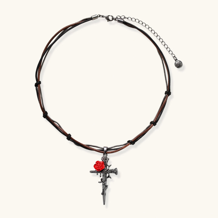 Gothic cross pendant with red enamel rose and thorn details on adjustable brown cord necklace against white background.